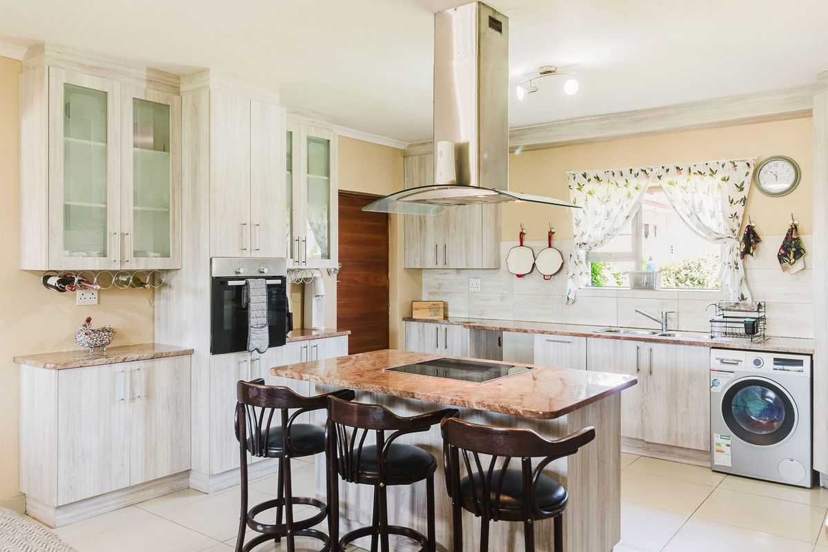 A well-appointed kitchen featuring light wood-grain cabinetry, stone countertops, a central island with a built-in hob, and integrated stainless steel appliances.
