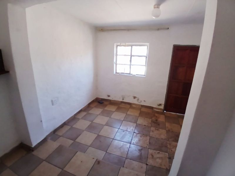 An empty bedroom featuring tiled flooring, a timber door, and a window with security bars, requiring cosmetic updates to the walls and flooring.