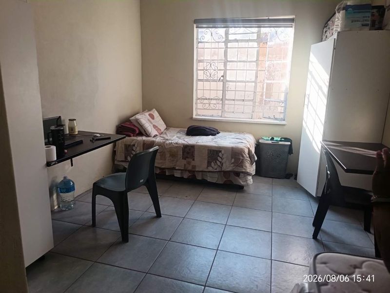 A functional bedroom featuring tiled flooring and a window fitted with security bars, offering a basic living space.