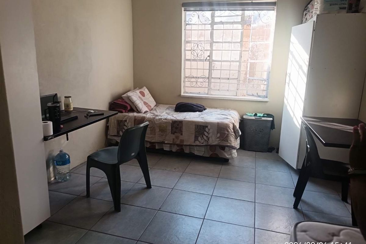 A functional bedroom featuring tiled flooring and a window fitted with security bars, offering a basic living space.