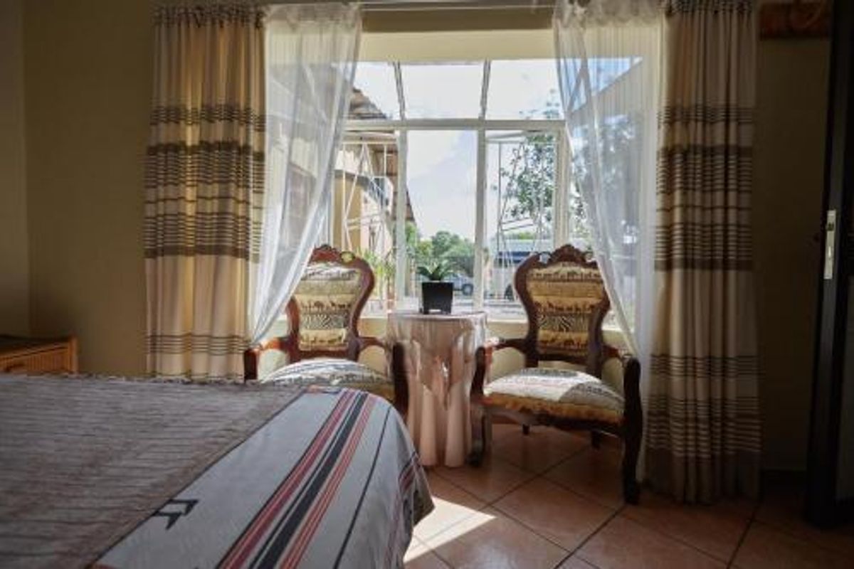 A bedroom featuring tiled flooring and a large window with integrated security bars, providing natural light and a view of the exterior.