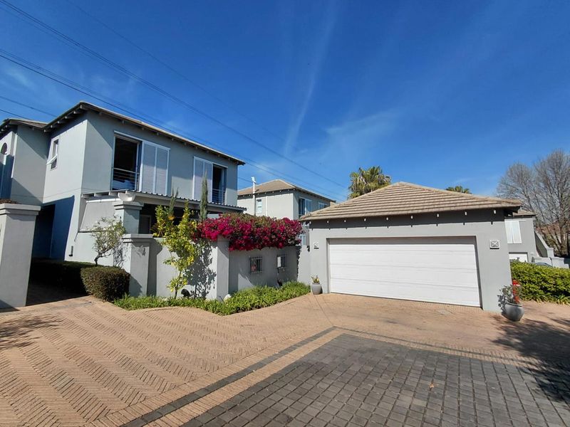 Front elevation of a cluster home featuring a paved driveway, double garage with white door, and well-maintained boundary wall with established landscaping.