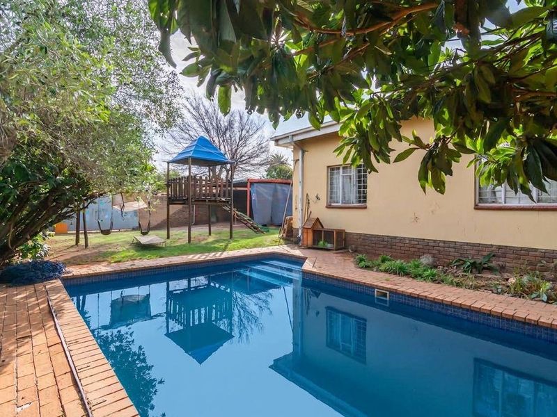 A backyard area featuring a swimming pool with brick coping, adjacent to the rear exterior wall of the house with security-barred windows.