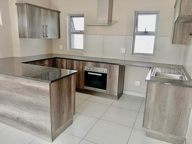 Modern kitchen featuring wood-look cabinetry, granite countertops, integrated stainless steel oven, electric hob, extractor fan, and tiled flooring.