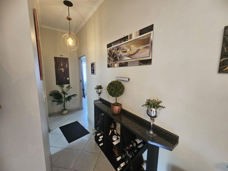 A well-lit hallway featuring tiled flooring, a decorative tongue and groove ceiling, and a modern pendant light fixture.