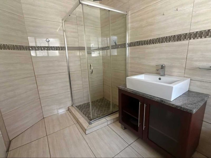 A modern bathroom featuring a glass shower enclosure, a vessel sink set on a granite-topped vanity cabinet, and neutral wall and floor tiling.