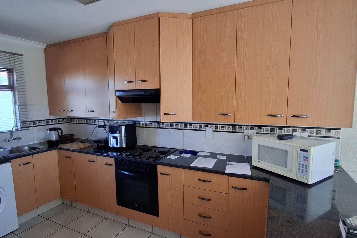 A functional kitchen featuring light wood-finish cabinetry, dark granite countertops, a built-in oven with hob, and a tiled backsplash.