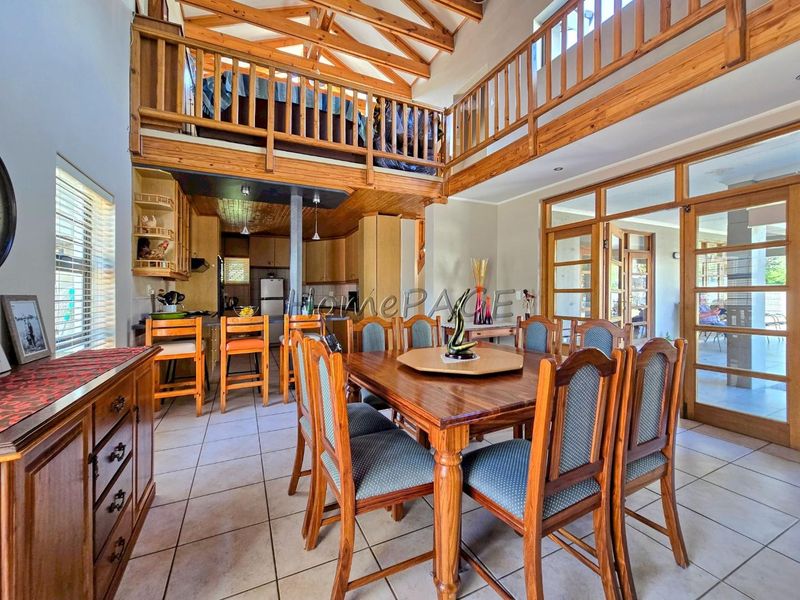 Open plan dining and kitchen area featuring exposed timber roof trusses, a mezzanine level with timber balustrade, and tiled flooring throughout.
