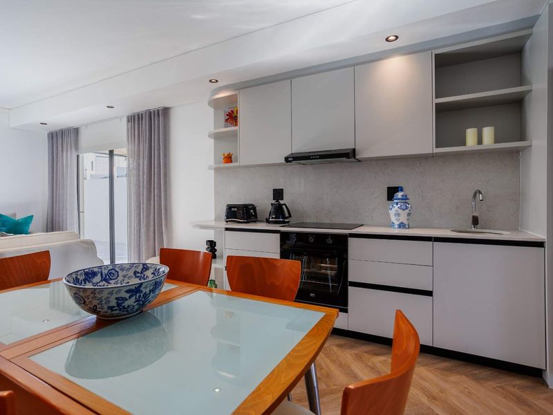 Modern open-plan kitchen and dining area featuring sleek cabinetry, stone countertops, integrated appliances, and stylish herringbone flooring with access to an outdoor space.