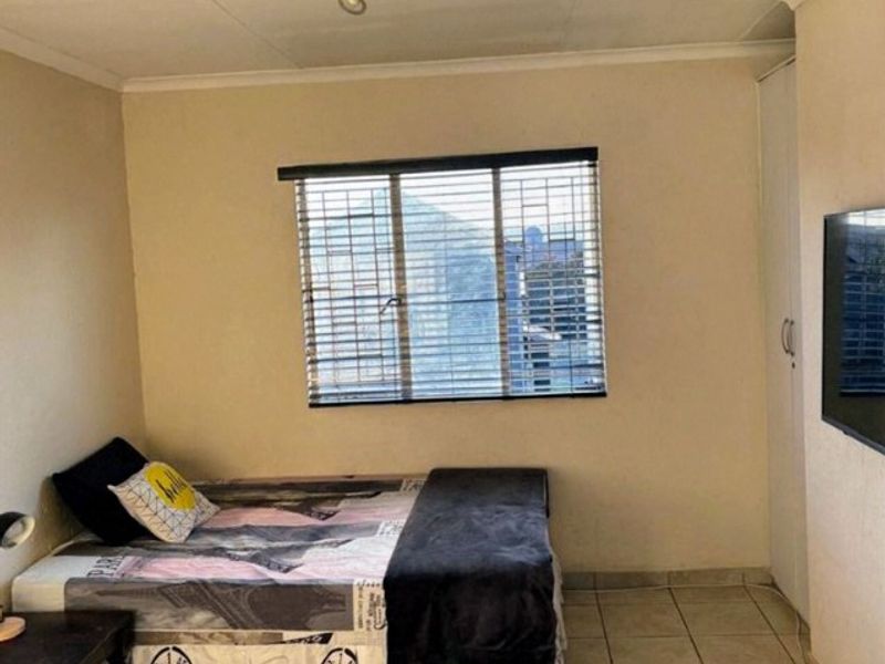 A functional bedroom featuring tiled flooring, a built-in wardrobe, and window blinds, offering a neutral space ready for personalization.