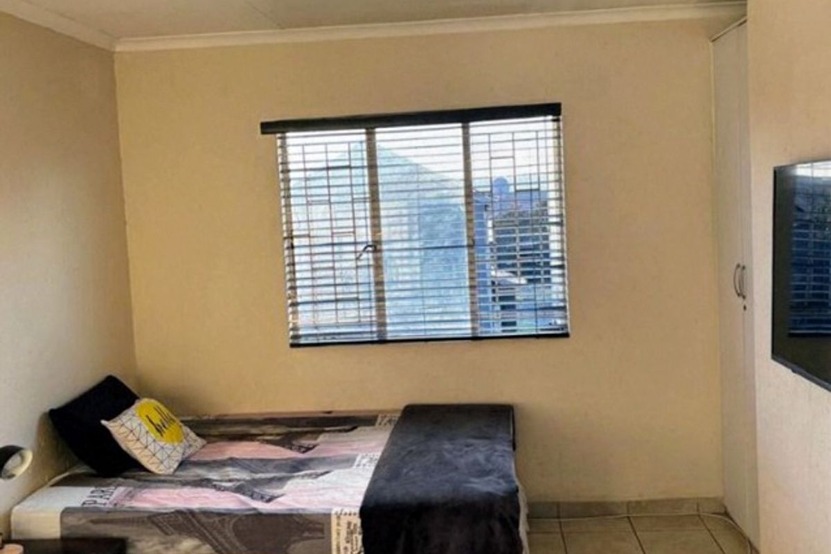 A functional bedroom featuring tiled flooring, a built-in wardrobe, and window blinds, offering a neutral space ready for personalization.