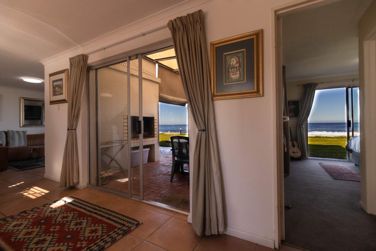 Living area featuring large sliding glass doors that open onto a covered patio with a built-in brick fireplace and direct ocean views.
