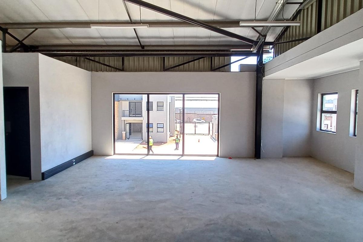 Spacious open-plan industrial unit featuring exposed steel roof trusses, concrete flooring, a brick feature wall, and large sliding doors leading to an exterior area.
