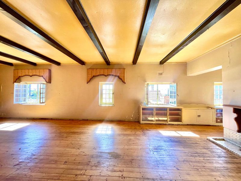 Spacious living room featuring exposed timber ceiling beams, original hardwood flooring, built-in cabinetry, and a brick fireplace hearth.