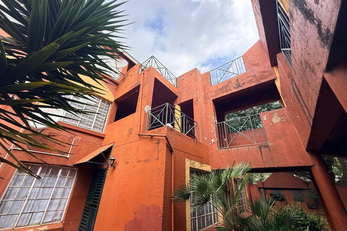 Exterior view of an apartment building complex featuring multi-level balconies, metal railings, and a textured facade with visible signs of weathering.
