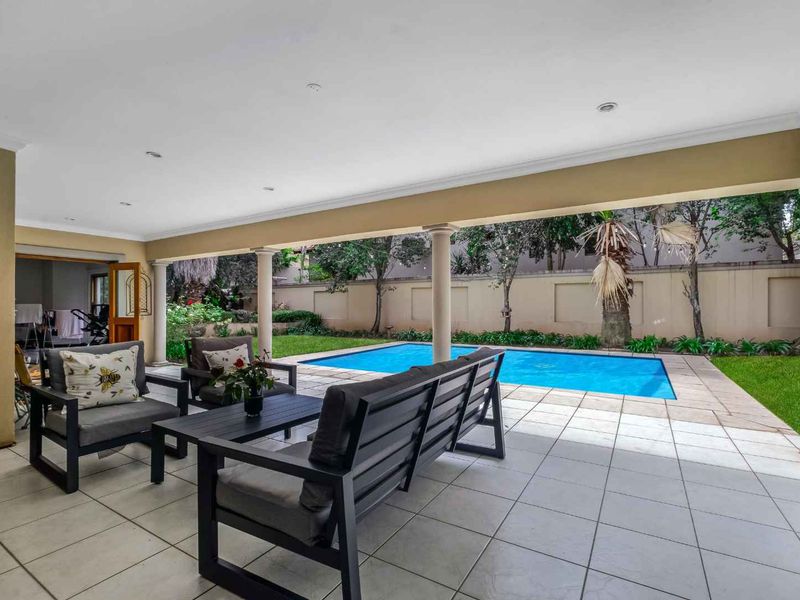 A spacious covered patio featuring tiled flooring and recessed lighting, overlooking a private swimming pool and landscaped garden area.