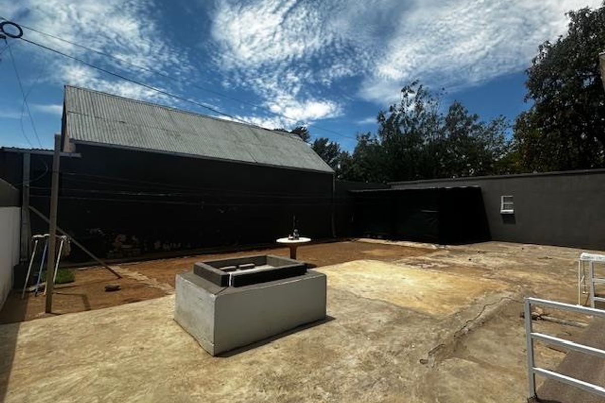 A spacious rear outdoor area featuring a concrete patio, a built-in fire pit or masonry structure, and perimeter boundary walls.