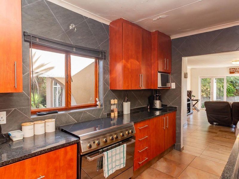 A functional kitchen featuring wooden cabinetry, granite countertops, a stainless steel stove, and tiled finishes, with an open flow into the adjacent living area.