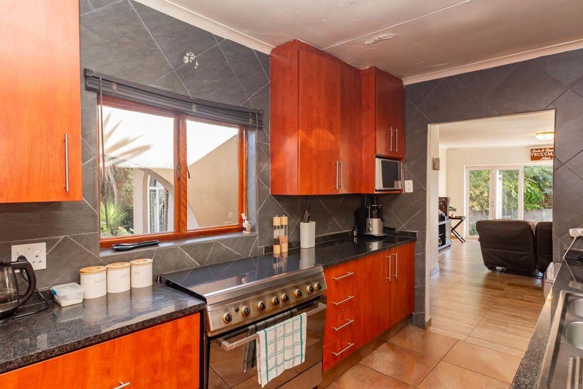 A functional kitchen featuring wooden cabinetry, granite countertops, a stainless steel stove, and tiled finishes, with an open flow into the adjacent living area.