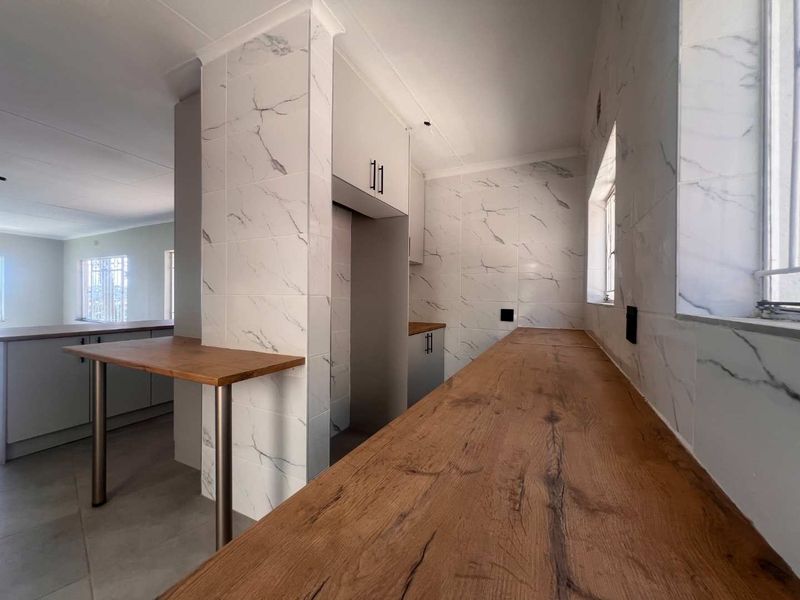 A modern, empty kitchen featuring marble-look wall tiles, wooden countertops, and built-in cabinetry with a breakfast bar area.