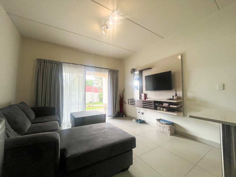 A bright living room featuring tiled flooring, a built-in media console, and a sliding glass door providing access to the outdoor area.