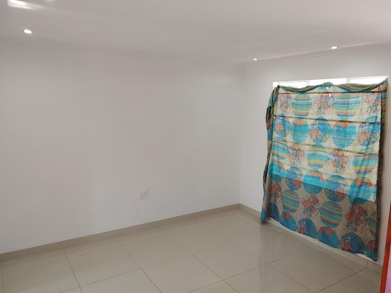 A clean, empty bedroom featuring neutral tiled flooring, recessed downlighting, and a window with existing window treatment.