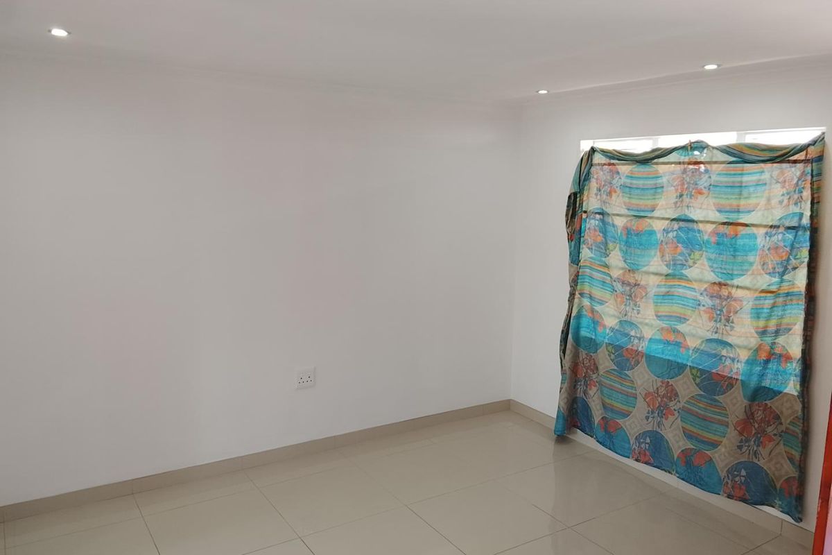 A clean, empty bedroom featuring neutral tiled flooring, recessed downlighting, and a window with existing window treatment.