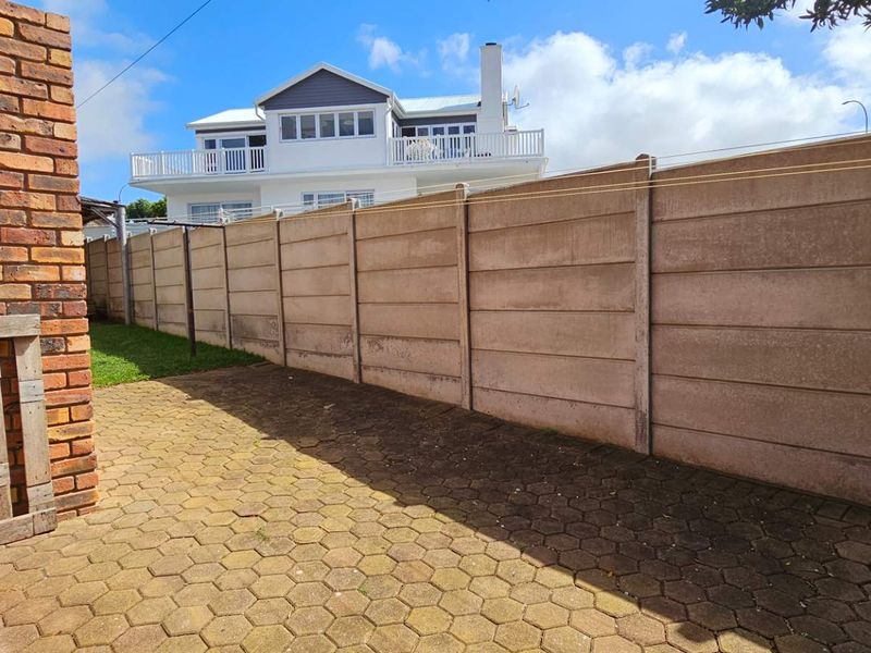 A rear outdoor area featuring a paved patio and a precast concrete boundary wall.