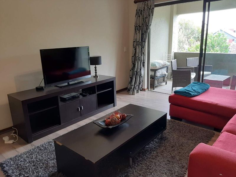 A living room featuring laminate flooring and a large sliding glass door providing access to an outdoor balcony area.