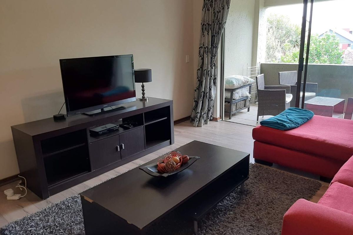 A living room featuring laminate flooring and a large sliding glass door providing access to an outdoor balcony area.
