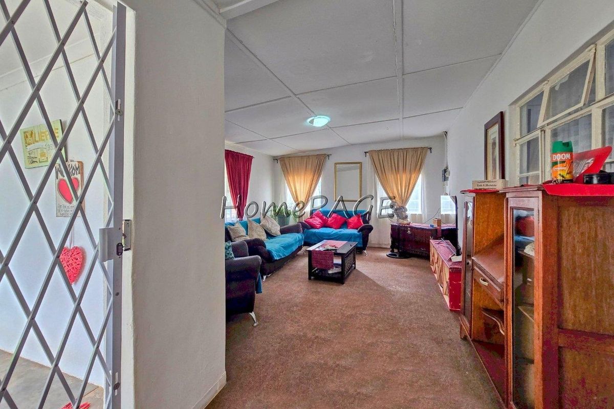 A living room featuring carpeted flooring, large windows, and a security gate at the entrance.