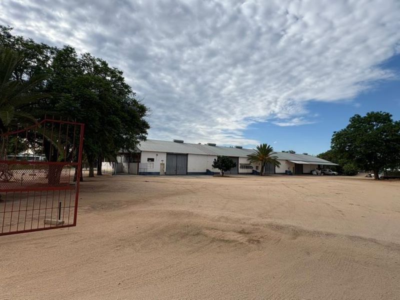A wide-angle view of a commercial property featuring large warehouse structures, a spacious gravel yard, and secure perimeter fencing.