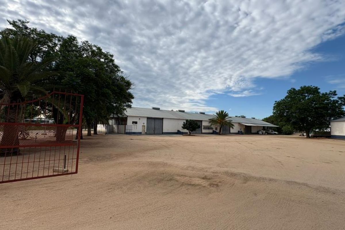 A wide-angle view of a commercial property featuring large warehouse structures, a spacious gravel yard, and secure perimeter fencing.