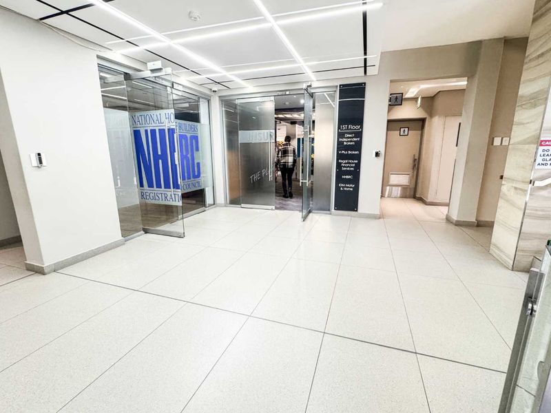 Modern commercial building entrance lobby featuring tiled flooring, glass entry doors, and clear directory signage for tenants.