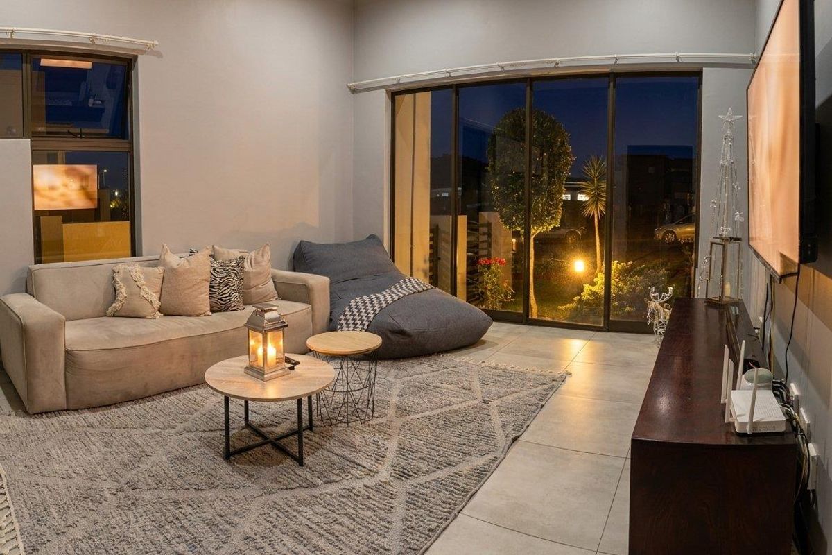 A modern living room featuring large sliding glass doors, tiled flooring, and neutral wall tones, providing a bright and comfortable space for relaxation.