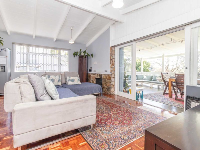 Spacious living room featuring beautiful parquet flooring, exposed beam ceilings, and a stone fireplace, with seamless flow to an outdoor patio through sliding glass doors.