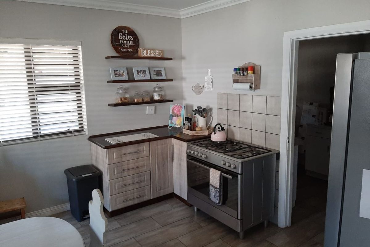 A functional kitchen area featuring wood-look cabinetry, a gas stove with oven, tiled splashback, and floating wall shelves.