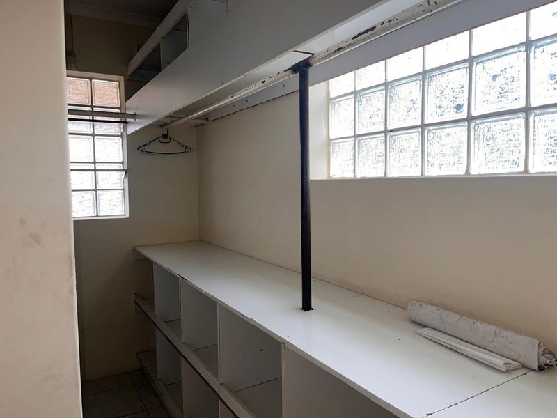 A functional utility or storage space featuring built-in shelving units, a hanging rail, and glass block windows providing natural light.