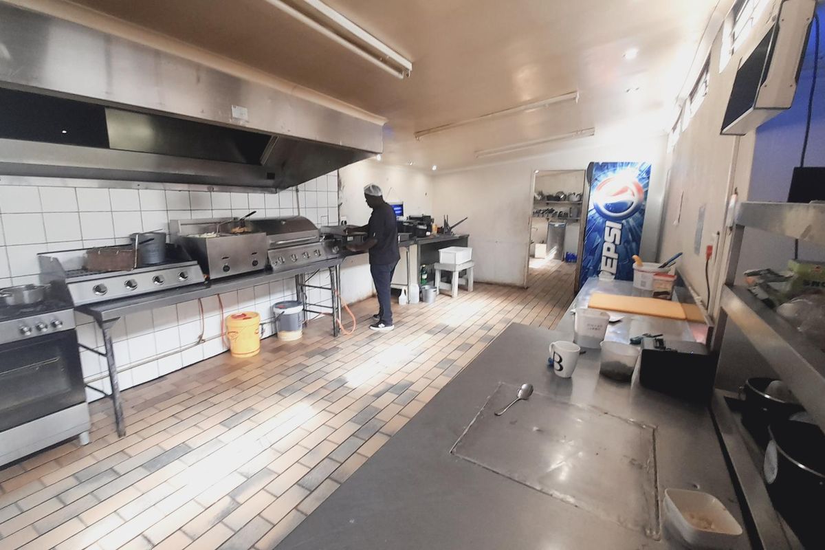Commercial kitchen featuring stainless steel prep counters, industrial gas range, and a large extraction canopy, suitable for high-volume food preparation.