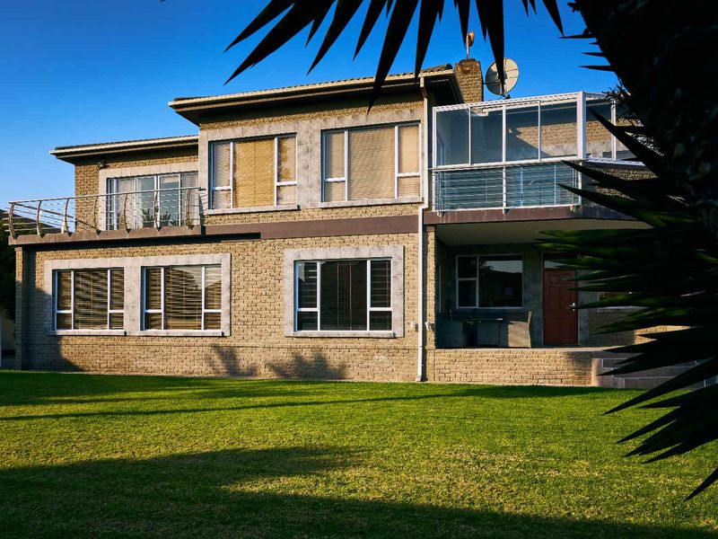 Rear view of a multi-story brick house featuring a spacious lawn, a covered patio, and an upper-level enclosed balcony.