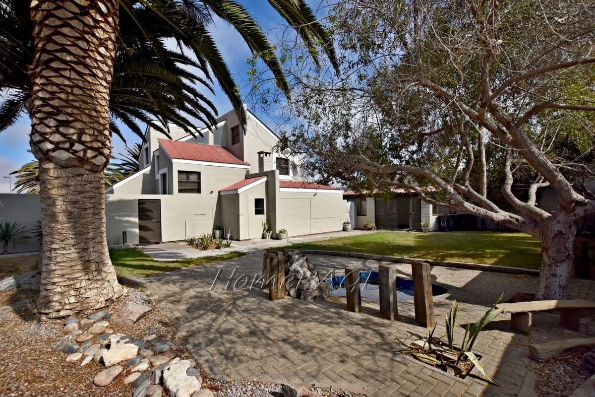 Rear view of the property featuring a paved patio area, swimming pool, and established garden with mature trees.