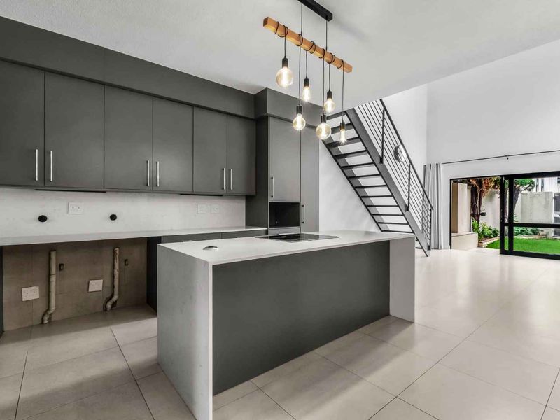 Modern open-plan kitchen and living area featuring sleek grey cabinetry, stone countertops, a central island, and direct access to the rear garden via sliding doors.