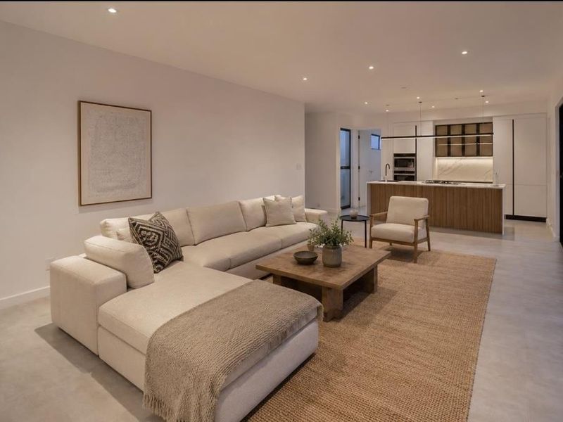 Modern open-plan living area featuring a sleek kitchen with island, stone benchtops, and large sliding glass doors leading to the exterior.