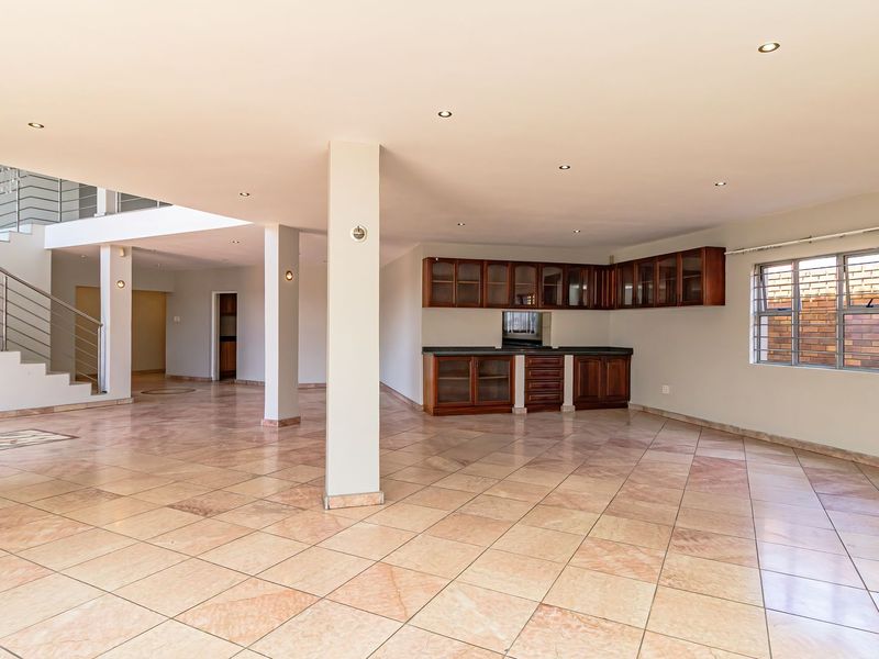 Spacious open-plan living area featuring tiled floors, recessed lighting, a modern staircase, and built-in cabinetry with stone countertops.