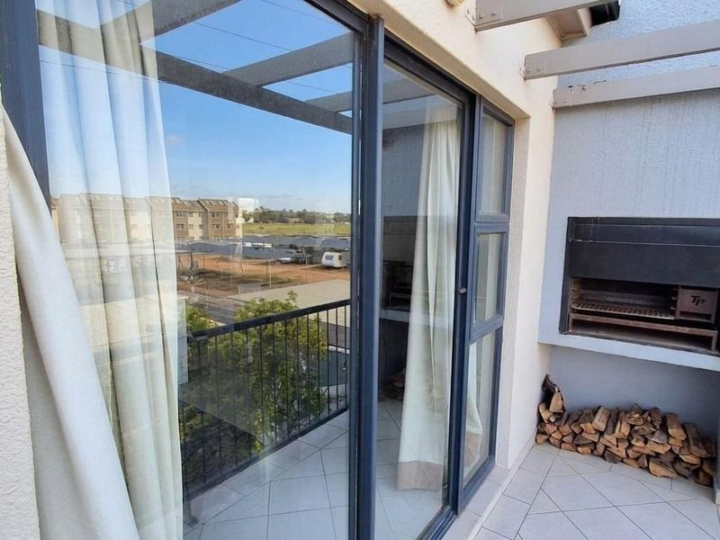 A covered balcony featuring tiled flooring, a built-in braai, and sliding glass doors, offering an outdoor space for relaxation and entertaining.