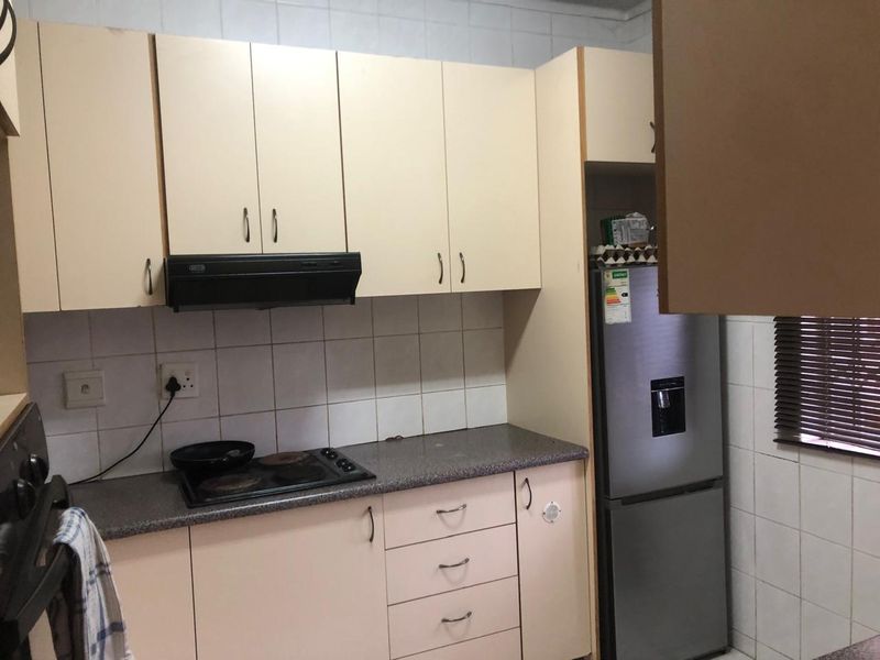A functional kitchen featuring light-toned built-in cabinetry, a tiled backsplash, and integrated cooking appliances including a hob and extractor fan.