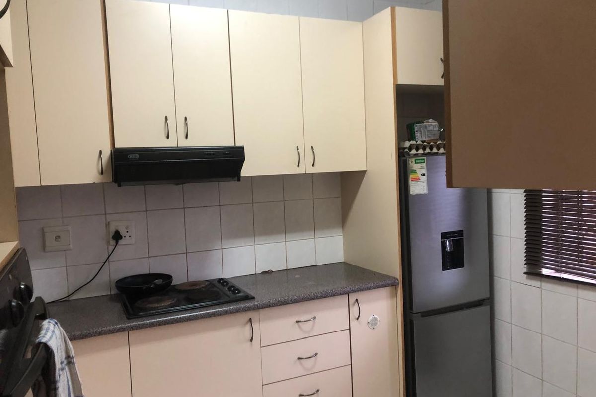 A functional kitchen featuring light-toned built-in cabinetry, a tiled backsplash, and integrated cooking appliances including a hob and extractor fan.