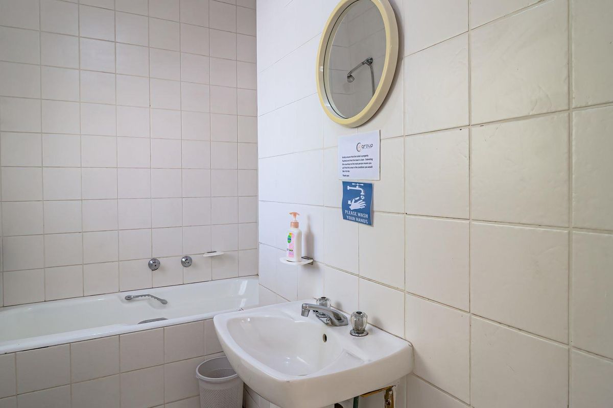A functional bathroom featuring a bathtub with shower head and a pedestal sink, finished with white ceramic wall tiles.
