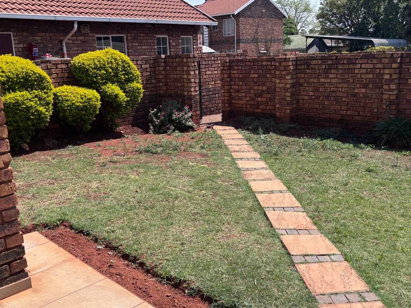 A private rear garden featuring a brick boundary wall, a paved walkway, and a small tiled patio area.