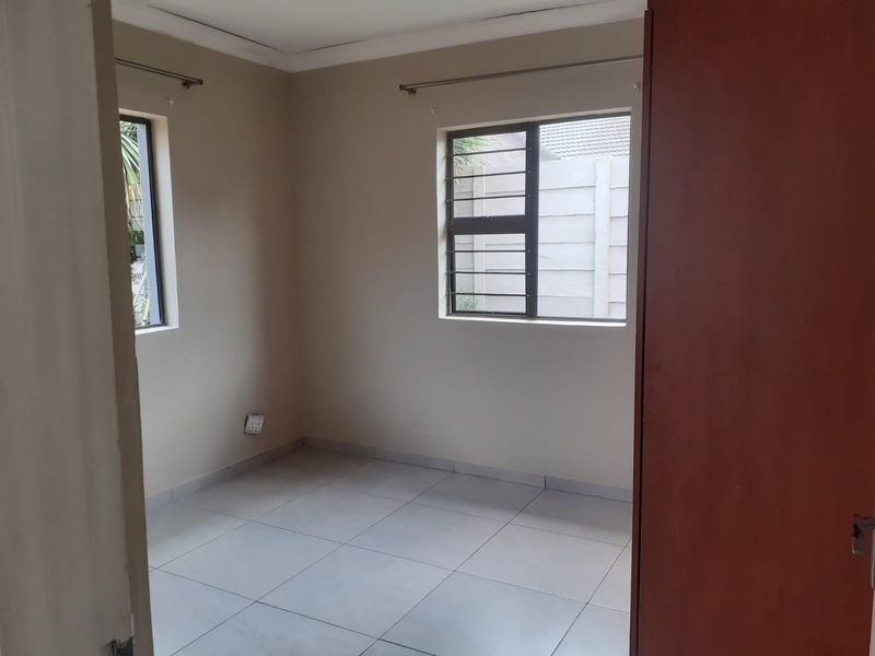 A clean, empty bedroom featuring neutral wall paint, tiled flooring, and security bars on the windows, providing a blank canvas for personalization.
